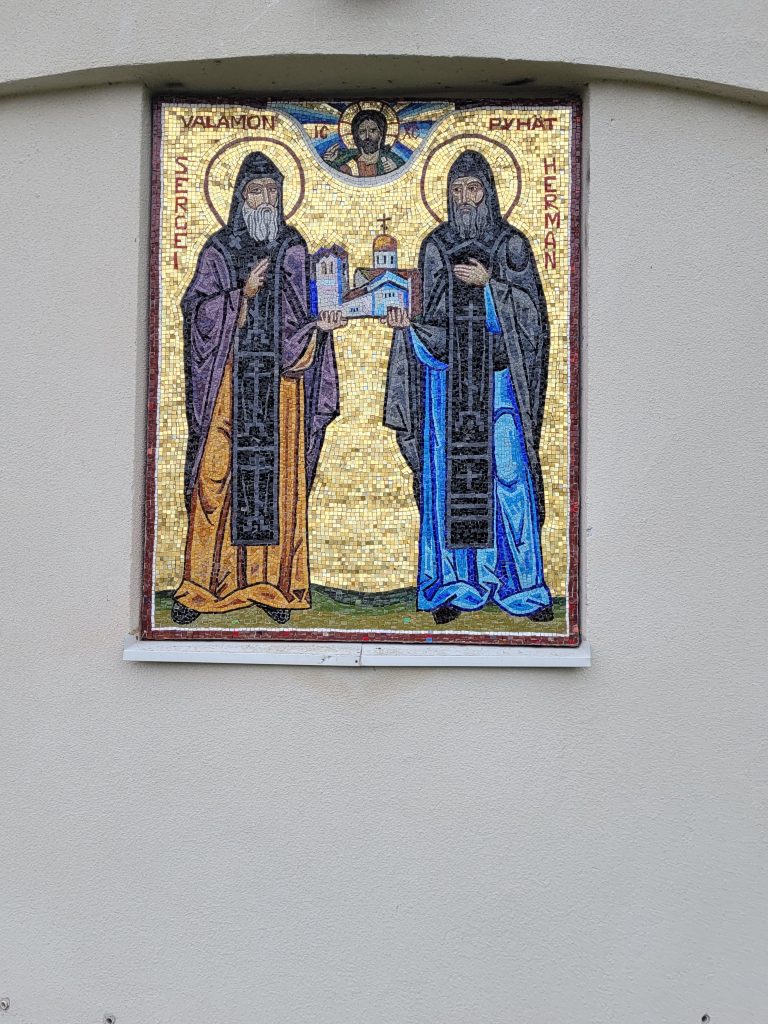 Mosaiikki-ikoniin tallennetut pyhittäjät Sergei ja Herman Valamolaiset tervehtivät pyhiinvaeltajia ja matkailijoita Uuden Valamon Kristuksen kirkastumisen kirkon seinustalla. (Kuva: Matti Pulkkinen)